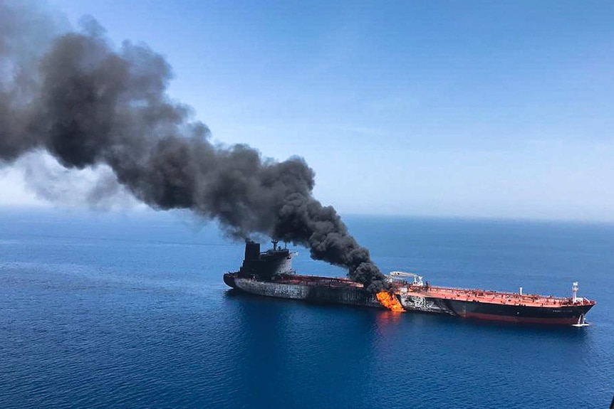 An oil tanker at sea is on fire with a large cloud of smoke coming out of it