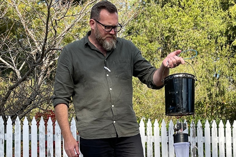 A man holding a bucket-shaped mosquito trap.