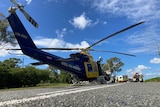 A rescue helicopter on a highway beneath a bright blue sky.