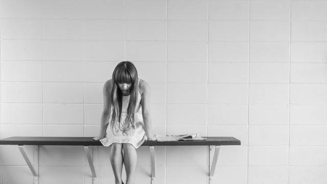 A woman in white dress and black shoes sits on changeroom bench with head down. Black and white image.