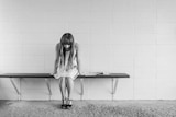 A woman in white dress and black shoes sits on changeroom bench with head down. Black and white image.