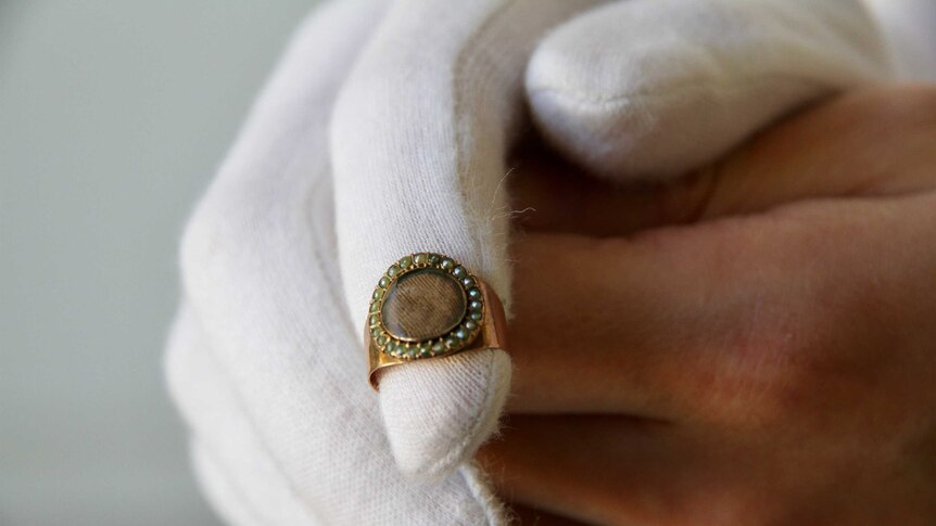 A gold ring made with small pearls around a woven hair compartment