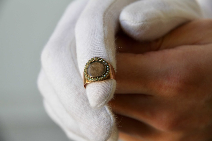 A gold ring made with small pearls around a woven hair compartment