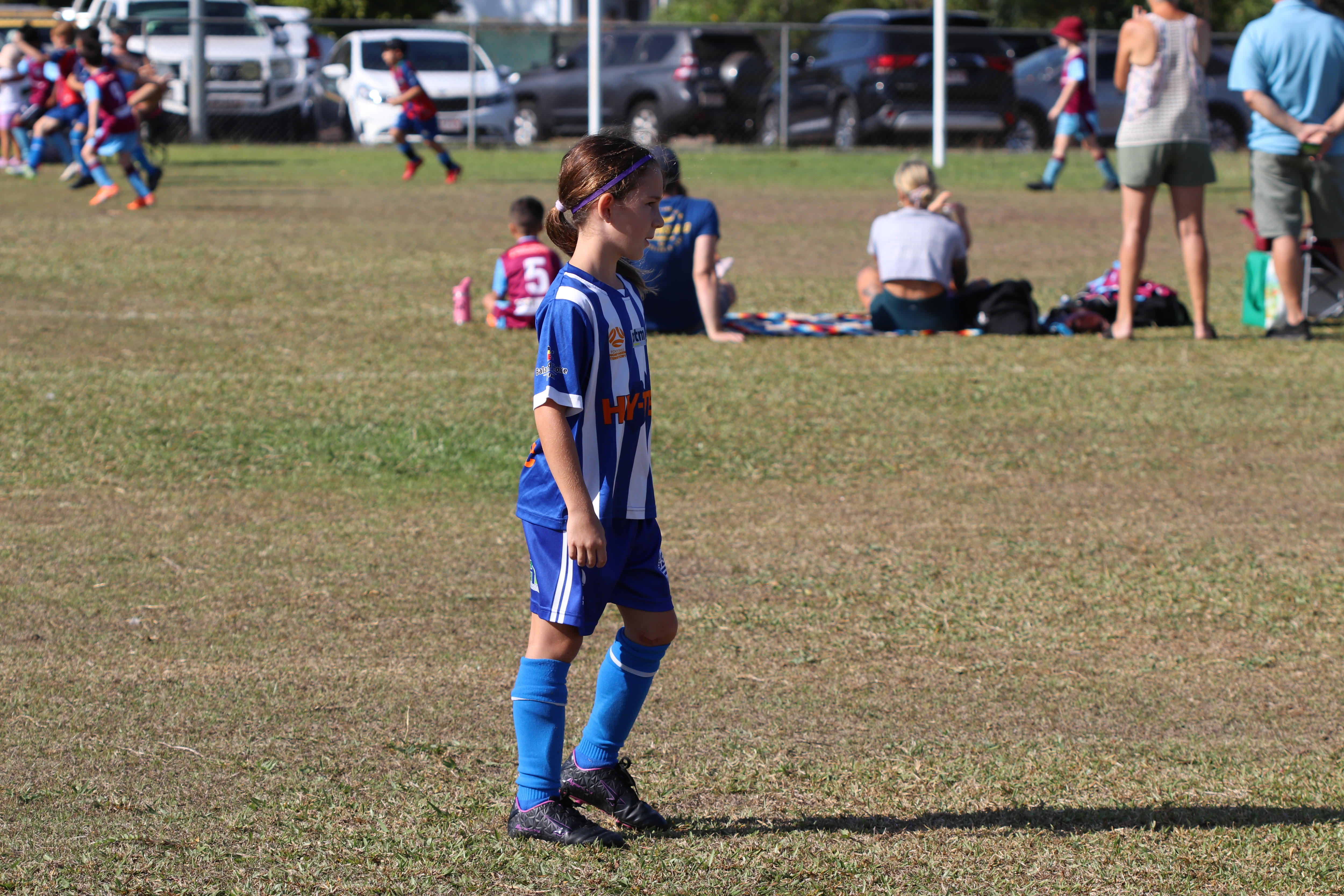 A young girl in a soccer uniform on a football field, ready to kick a ball