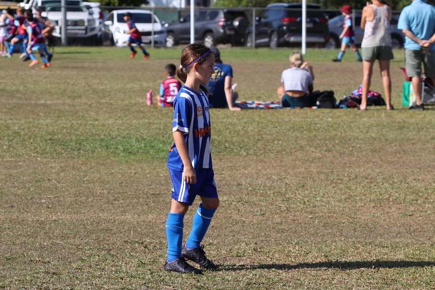 A young girl in a soccer uniform on a football field, ready to kick a ball
