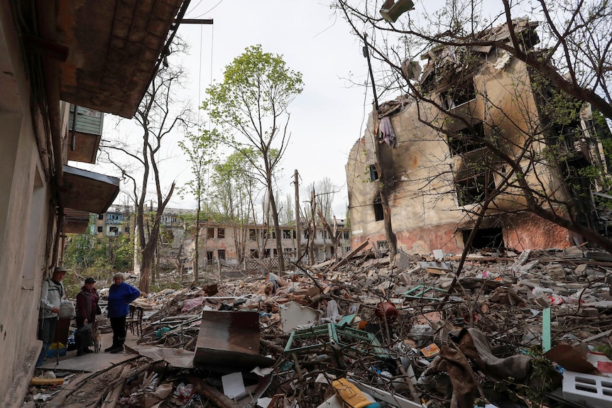 Three people stand beside a destroyed building.