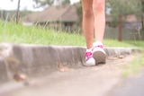 The legs of a young girl wearing pink sneakers, walking near a gutter