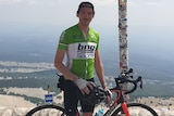 A man in green bicycle gear stands with a bike in front of a sign that reads "Somme du Ventoux".