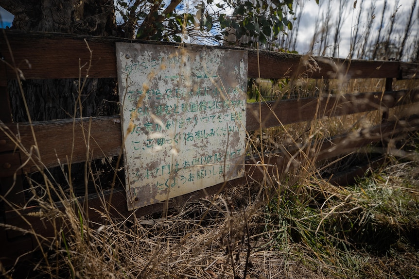 sign written in Japanese on fence. Very faded with paint peeled away.