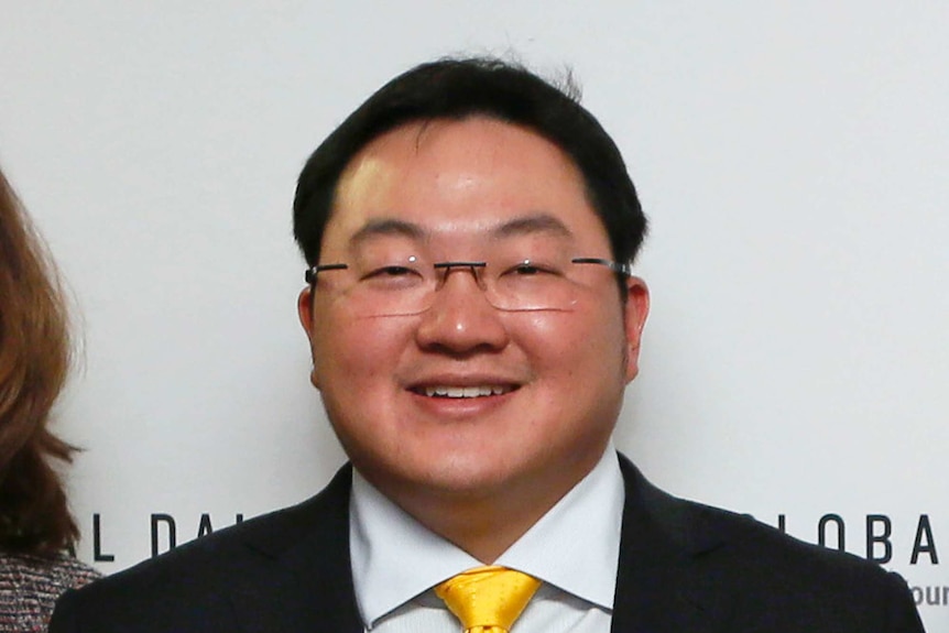 A man of Asian appearance smiling in suit with yello tie and pocketsquare.