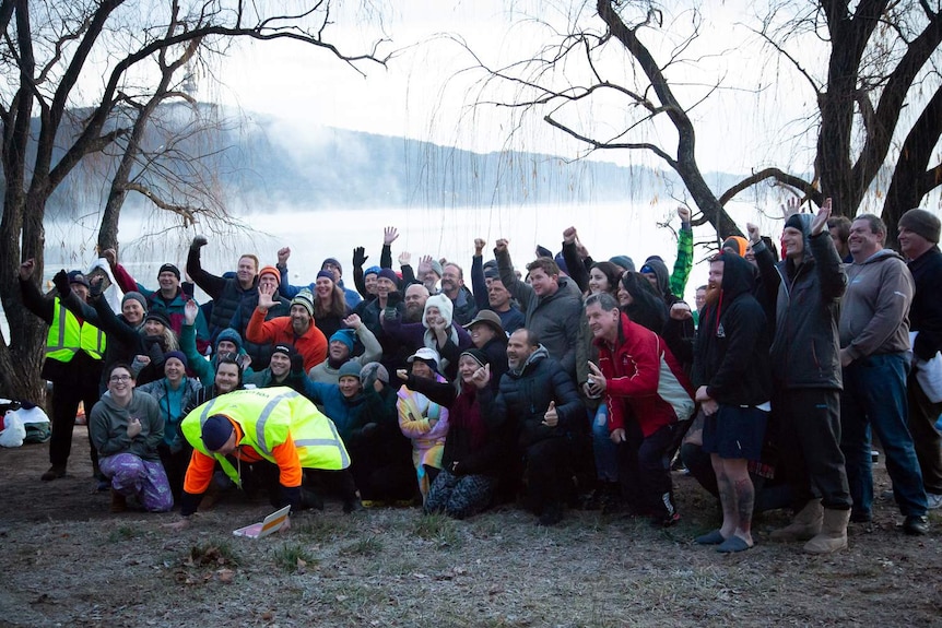 Swimmers group together for a photo beside the lake.