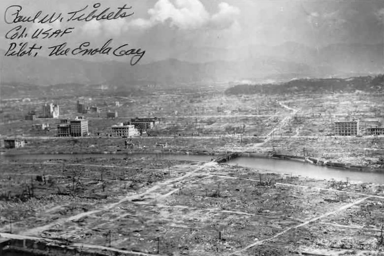 A black and white photo shows the remains of a city with only a few odd buildings still standing.