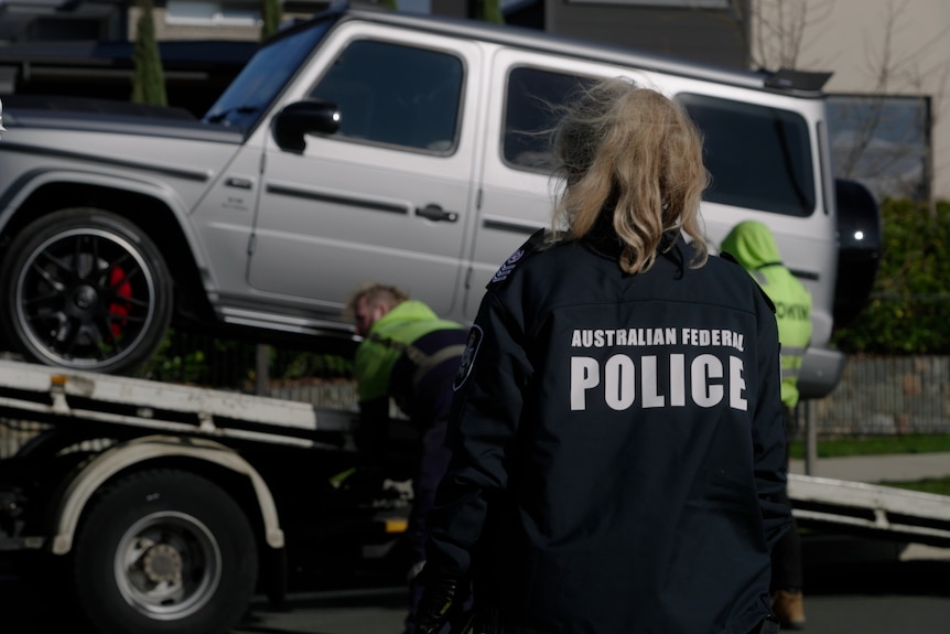 A police officer stands in front of a car as it is towed away 