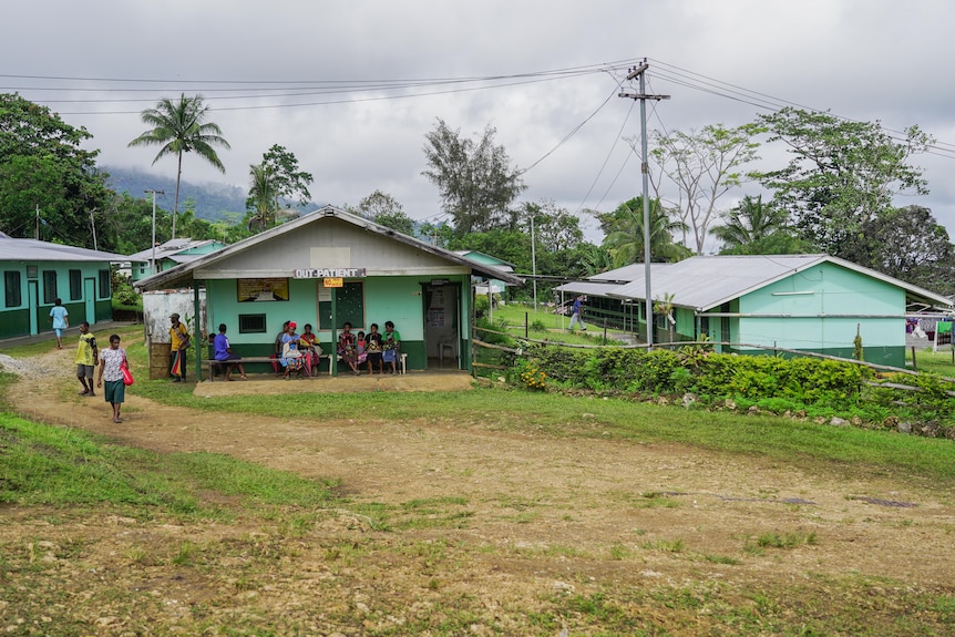 People stand outside two weatherboard buildings surrounded by palm trees