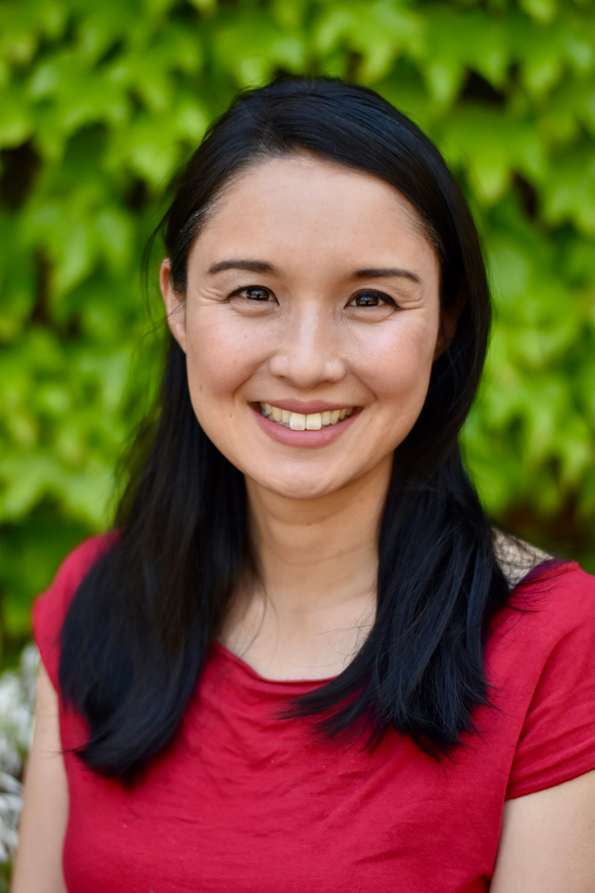 An Asian Australian woman in her early 40s, with long black hair and wearing a red blouse, smiles at the camera.