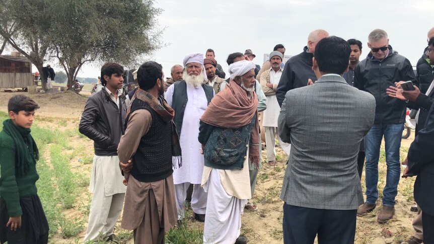 A group of men on a farm in Pakistan gather around to listen to a talk