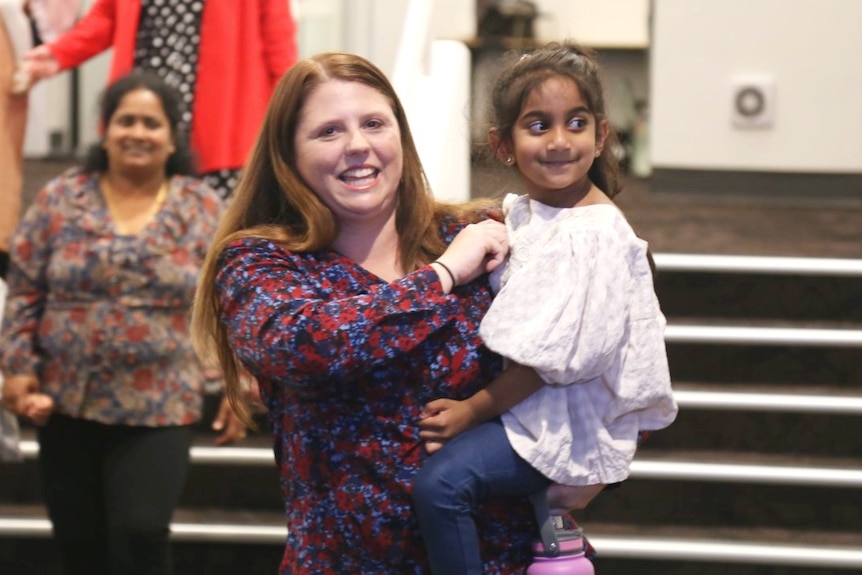 A smiling woman holds a little girl.