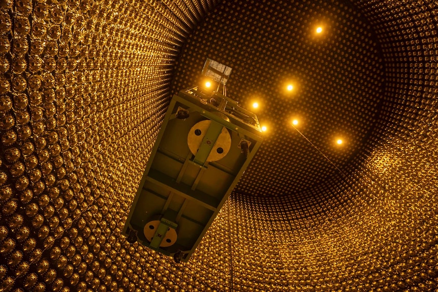 Shot looking up of platform on pulley inside circular observatory with walls of golden photomultiplier tubes.