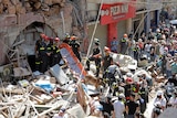 French and Lebanese firemen aided by a sniffer dog search in the rubble of a building as crowds watch.