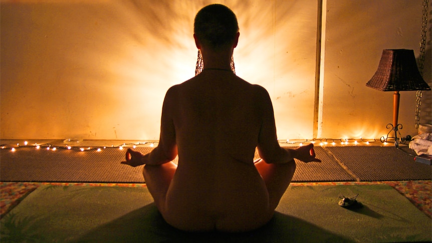 A woman does nude yoga in a lotus pose