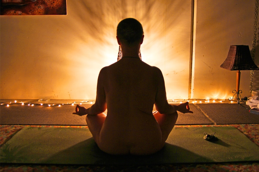 A woman does nude yoga in a lotus pose