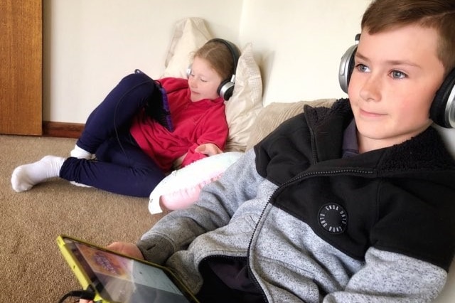 Two children sitting on cushions on floor listening to podcast on ipad.