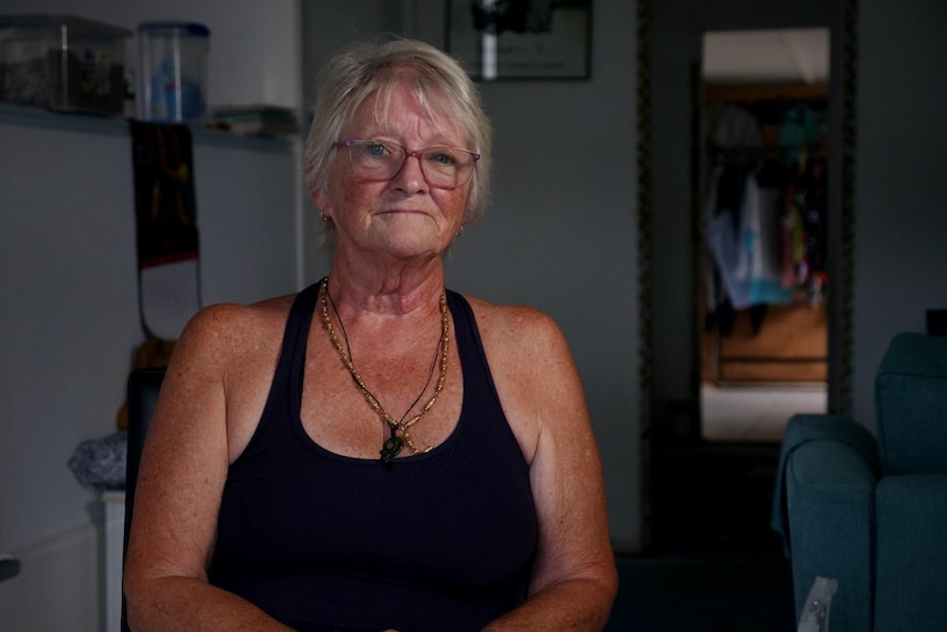 A woman with short blonde hair, glasses in a black singlet inside a house