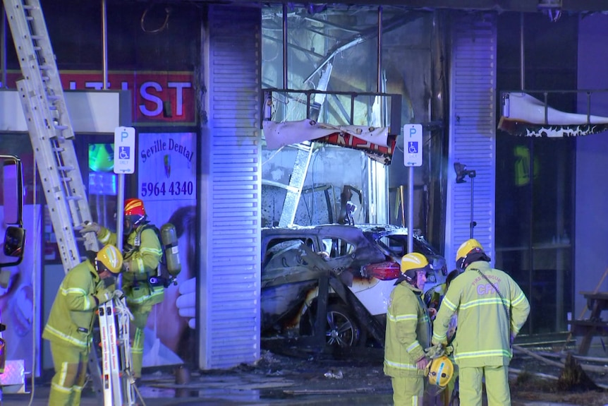 Fire fighters stand out the front of a tobacco store following a fire with a car through the store front.