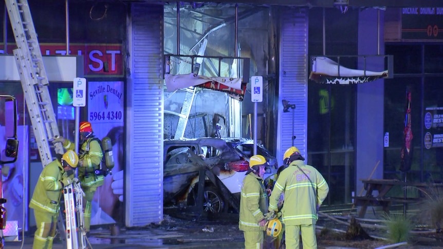 Fire fighters stand out the front of a tobacco store following a fire with a car through the store front.