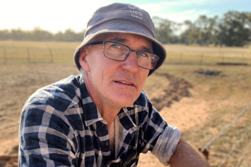 A man is on a farm leaning on a fence with a hat on