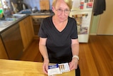 A woman sits at a kitchen table with a medicine kit in her hand.