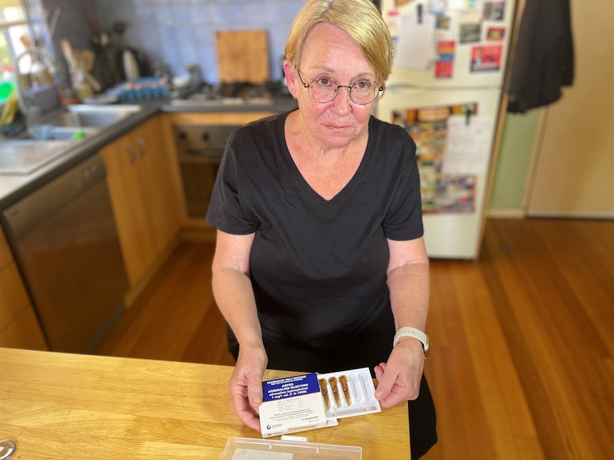 A woman sits at a kitchen table with a medicine kit in her hand.