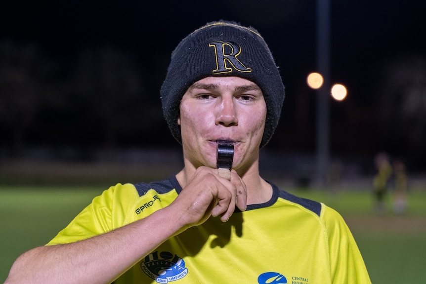 a young man looks at the camera and blows a whistle.