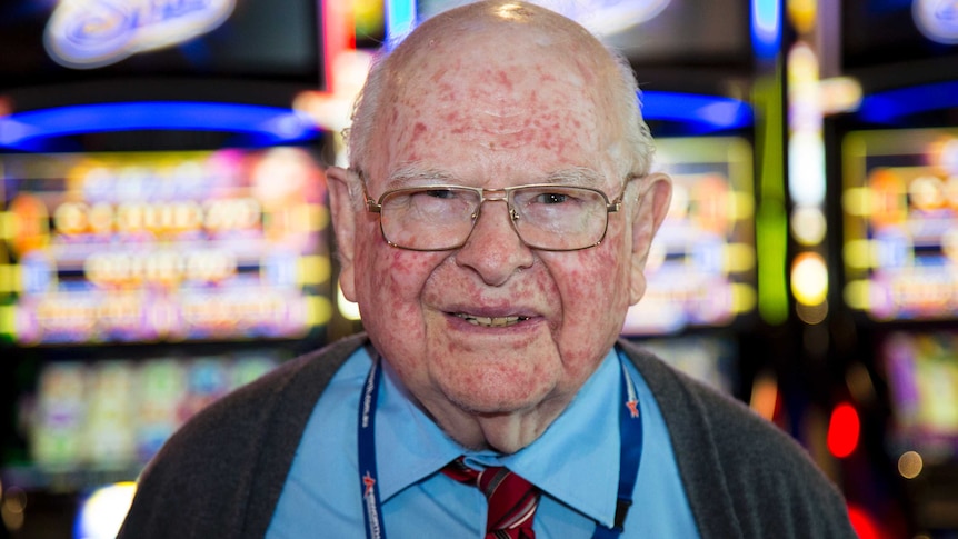 Len Ainsworth smiles as he stands in front of a row of flashing Ainsworth Quad Shot poker machines.