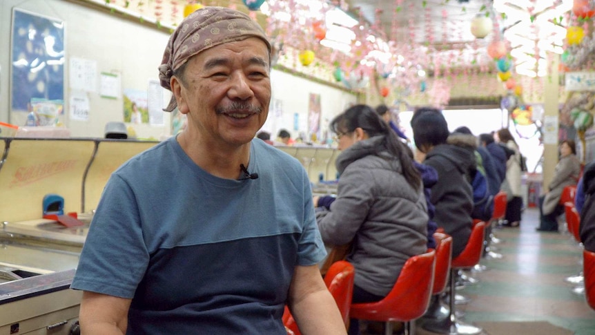 Akinori Egawa sits on a chair smiling and waiting to do a TV interview.