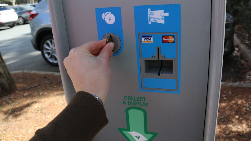 A person putting a coin into a pay parking machine.
