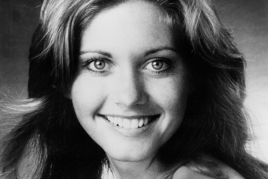 A black and white headshot of Olivia Newton-John smiling