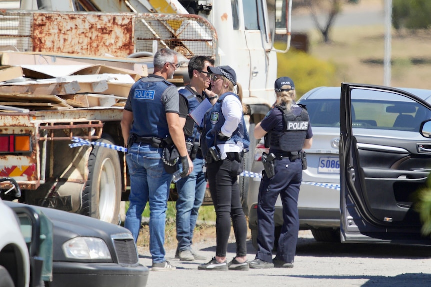 Four police officers stand chatting next to a truck and three parked cars