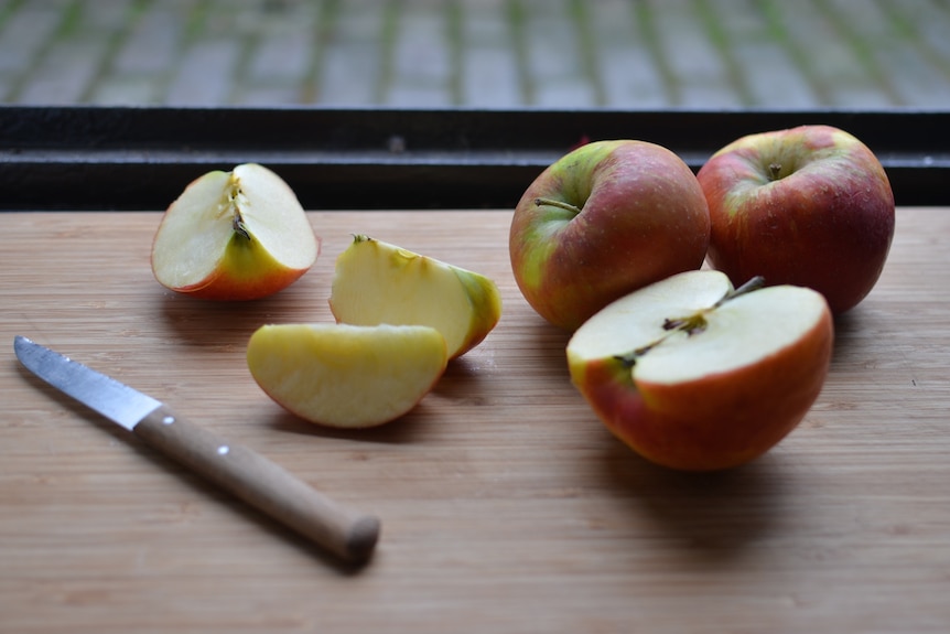 An apple on a chopping board, cut into wedges and slices. Cut fruit can be easier to eat.