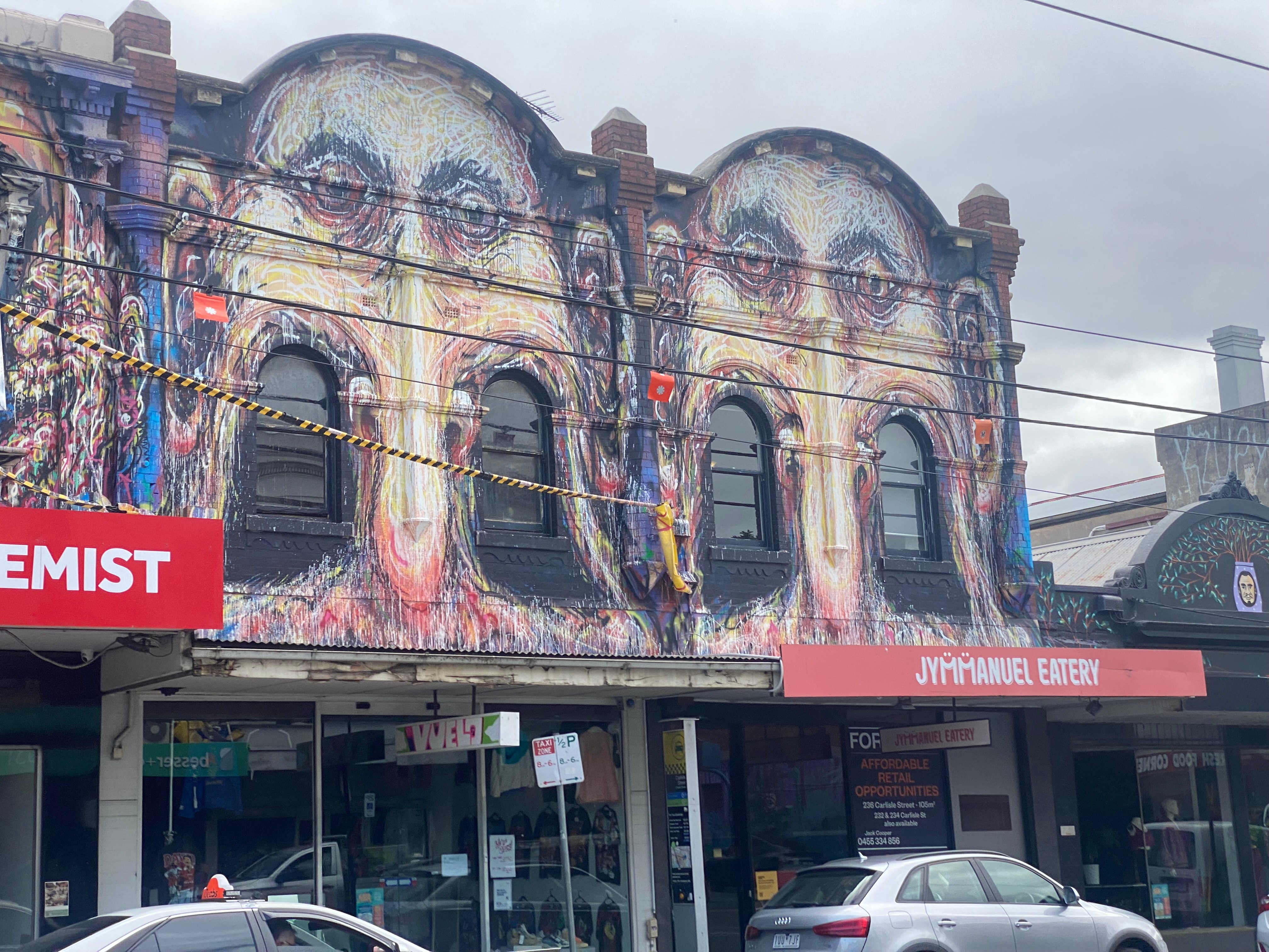 A mural showing distorted faces covers the exterior second storey facade of businesses.