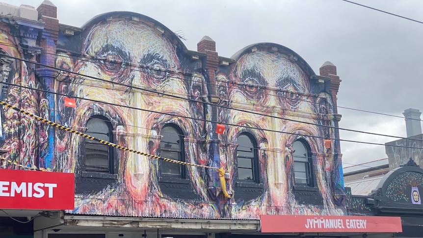 A mural showing distorted faces covers the exterior second storey facade of businesses.