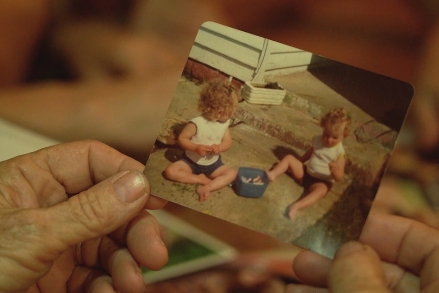 Hands hold a photo of toddler twin girls