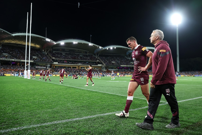 A Queensland State of Origin player walks around the pitch with a trainer after leaving play during a State of Origin game.