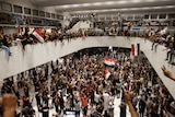 Hundreds of protesters inside the Iraqi parliamentary building. Some wave Iraqi flags.