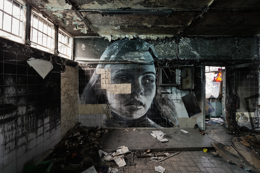 A picture of a woman looking back over her shoulder is painted over crumbling tiles