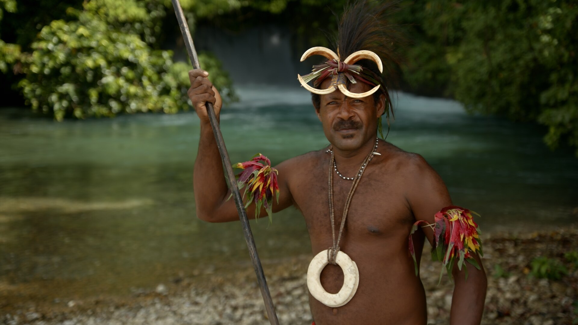 Mid shot of PNG man in traditional dress on a sunny day with a river in the background