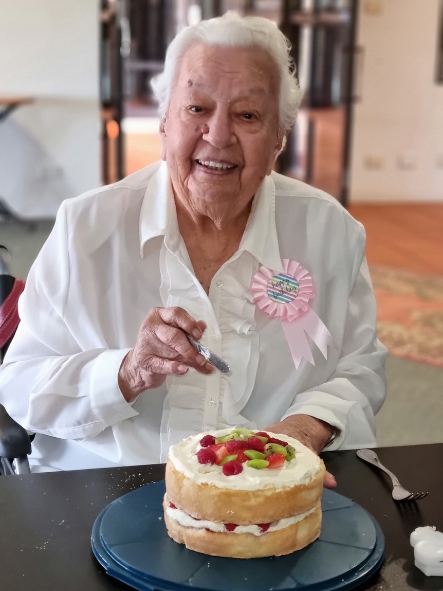 An elderly woman smiles wearing a pink ribbon reading "Birthday"