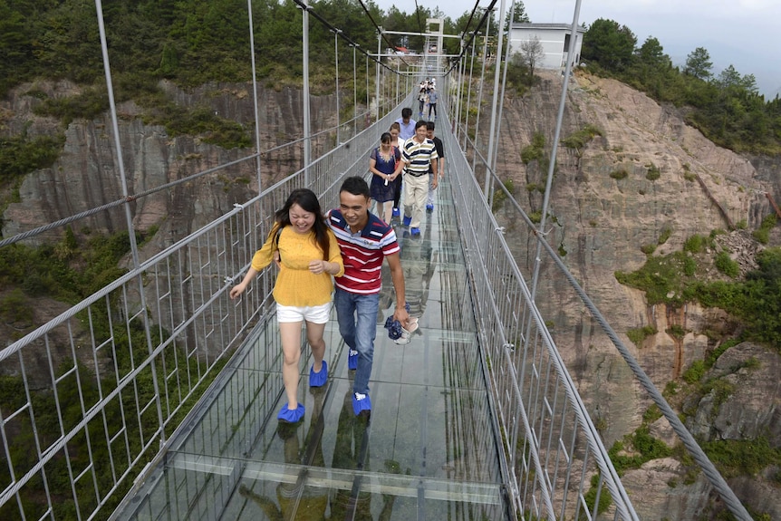 Tourists walk along the glass bridge in Shiniuzhai park in China with shoe coverings.