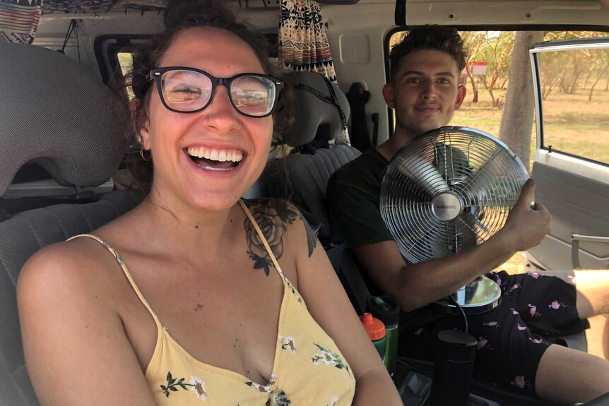 A young woman wearing glasses and a young man with a fan on his lap sit in a vehicle.