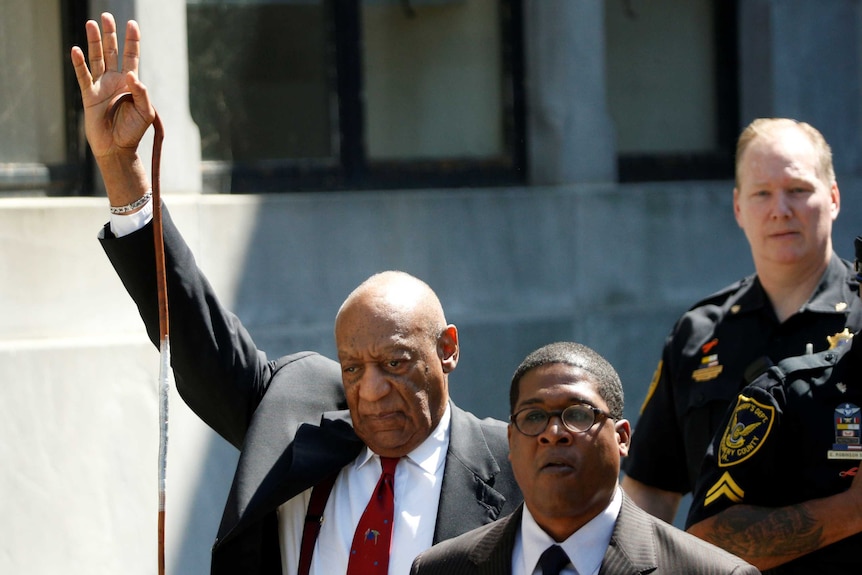 Bill Cosby holds one arm in the air as he leaves court.